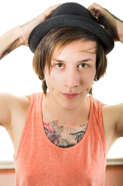 Headshot young hispanic male wearing black hat, red sleveless shirt with tattoos on chest and arms, punk rock insipired look, posing for camera