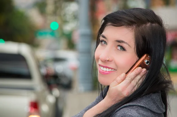 Classy latina model wearing smart casual clothes walking in urban street talking on her mobile phone and looking backwards towards camera