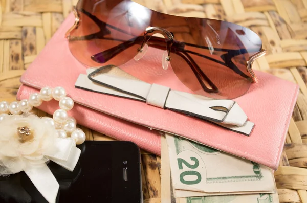 Womans purse pink color lying flat with accessories such as mobile, makeup, keys and money spread out in front