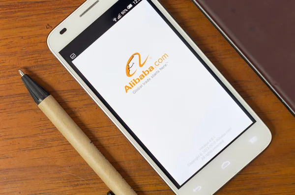 QUITO, ECUADOR - AUGUST 3, 2015: White smartphone lying on desk with Alibaba screen open next to a pen, business and communication concept