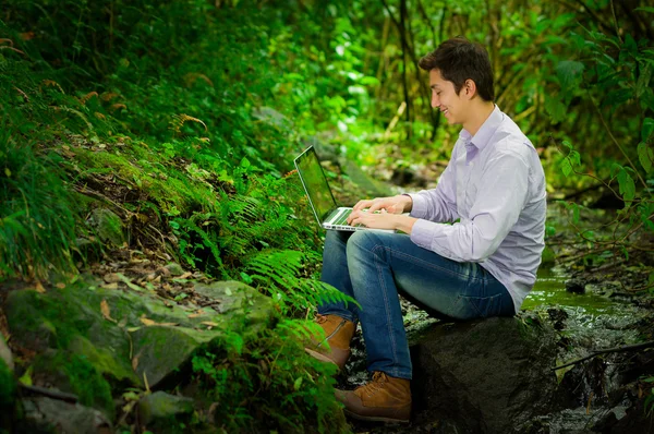 Young handsome man using laptop with great internet connectivity in the jungle