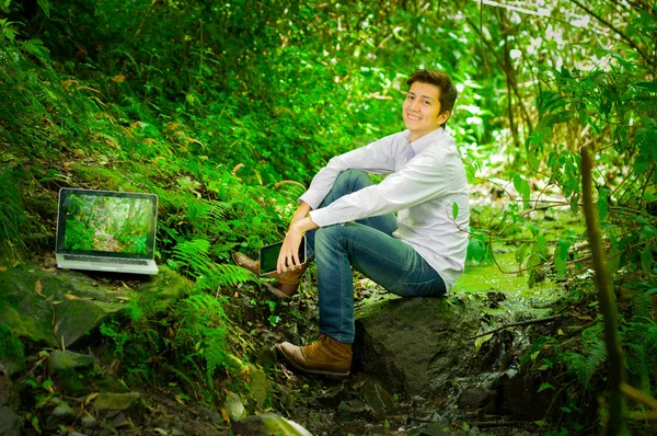 Young handsome man working with laptop and relaxing in the jungle