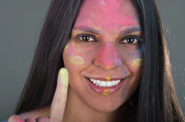Beautiful young brunette girl painting her face with colorful powder