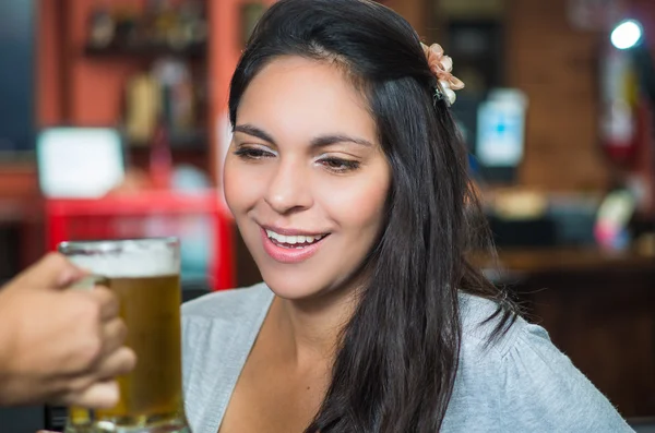 Brunette model in bar environment receiving glass of beer and smiling