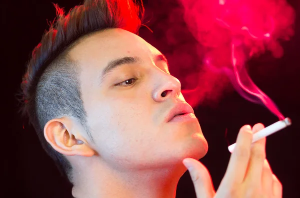 Hispanic male headshot posing with serious facial expression and smoking a cigarette smoke visible