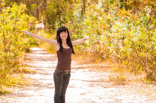 Pretty brunette with tattoos wearing rock inspired clothing walking on dirt road in forest environment enjoying nature
