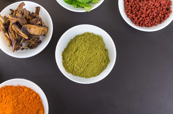 Beautiful colorful display of different spices green orange brown in white bowls, shot from above angle, grey background
