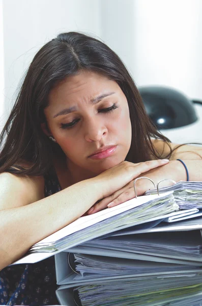 Hispanic brunette office woman working sitting by desk with paper file archive open and looking tired