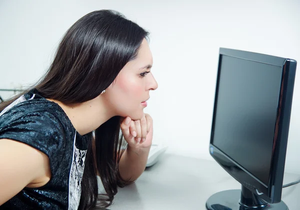 Hispanic brunette sitting by office desk working on computer with occupied and worried facial expression