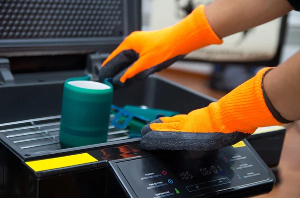Hands wearing orange gloves working on black print screen machine