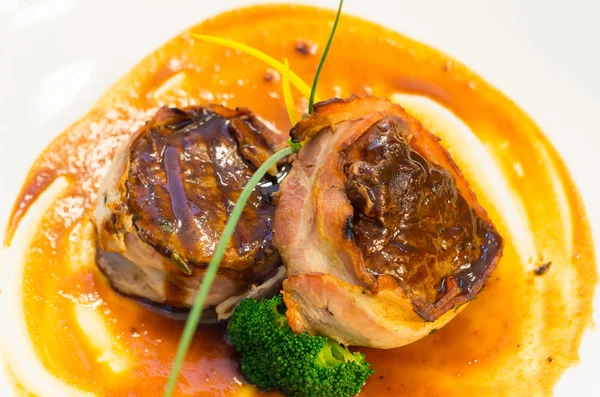 Delicious tenderloin steak wrapped in bacon and cooked to perfection, placed on orange plate with some vegetable elements, elegant presentation