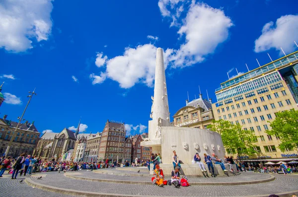 Amsterdam, Netherlands - July 10, 2015: Dam Square on a beautiful sunny day, tall monument and historical buildings around plaza