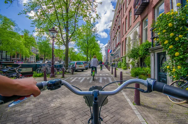 Amsterdam, Netherlands - July 10, 2015: Bikers point of view as bicycling through city streets on a beautiful sumer day