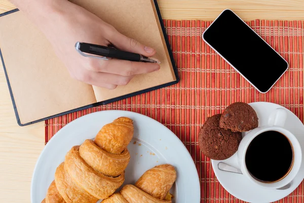 Table with breakfast, cell phone and notebook