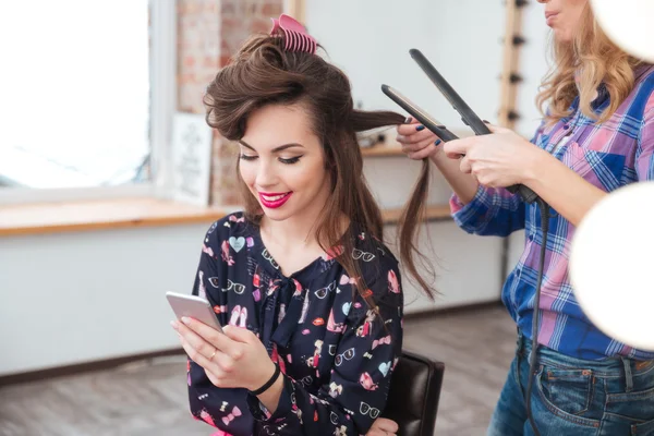Hairdresser applying straightener for long hair of smiling  woman