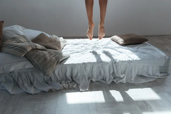 Slim legs of young woman flying in air above bed