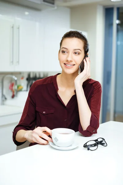 Woman drinking coffee and talking on mobile phone at kitchen