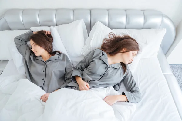 Two attractive young sisters twins sleeping in bed
