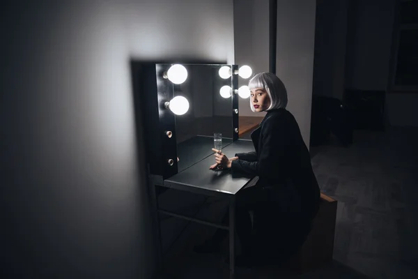 Thoughtful blonde woman drinking champagne near mirror in dressing room