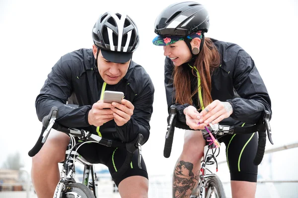 Happy couple on bicycles resting and using smartphone