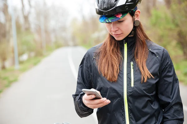 Thoughtful woman in bicycle helmet using cell phone