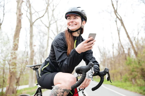 Happy woman in cycling helmet on bicycle using smartphone