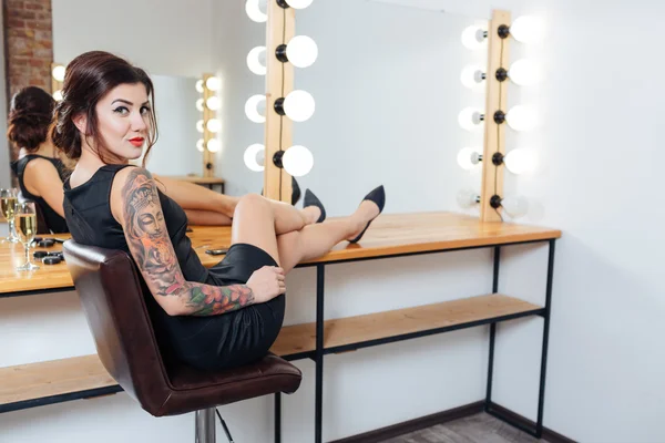 Tattooed woman sitting in dressing room with legs on table