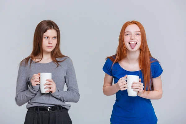 Two happy joking and sad frowning young women drinking tea