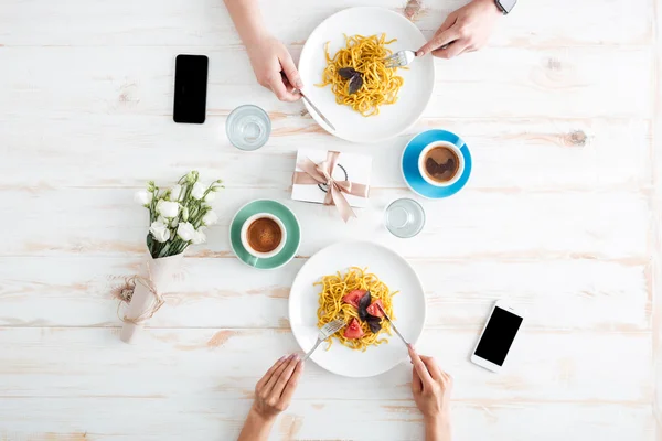Hands of young couple eating pasta together on wooden table
