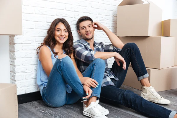 Happy couple sitting on floor around boxes after buying house