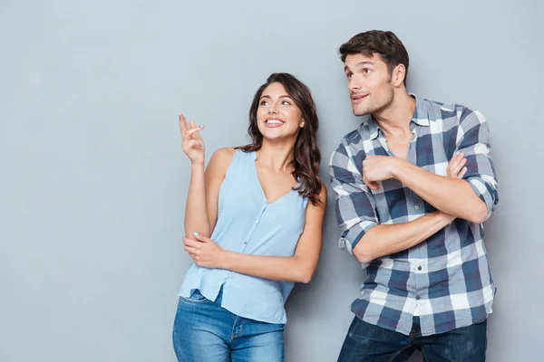 Smiling couple standing and pointing at something over gray background