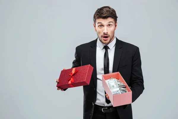 Surprised young businessman holding opened gift box with money