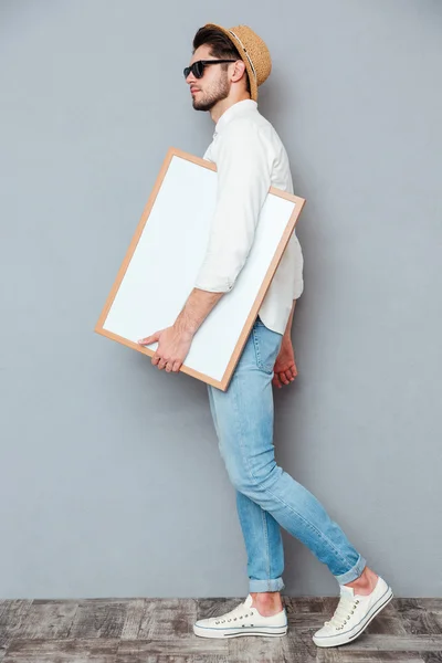 Attractive young man walking and holding blank white board