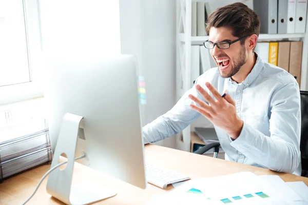 Angry mad young businessman working with computer and shouting