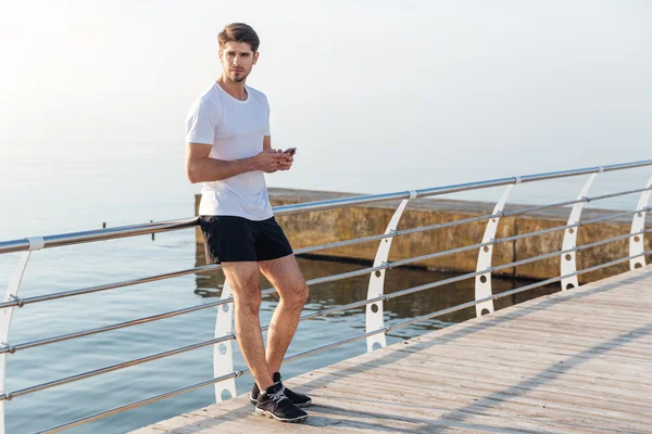 Man athlete standing on pier and using smartphone