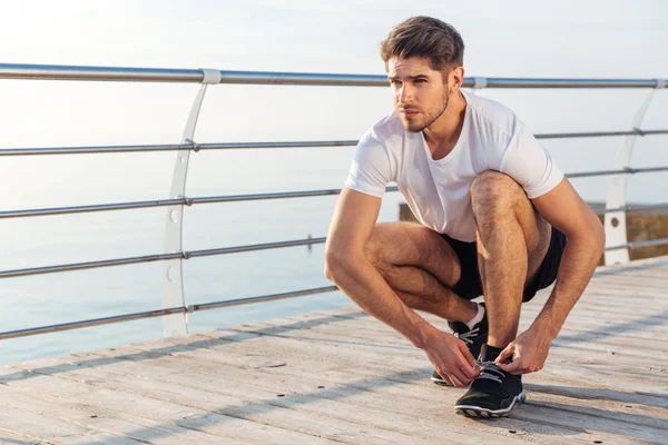 Man athlete laces his sneakers on pier