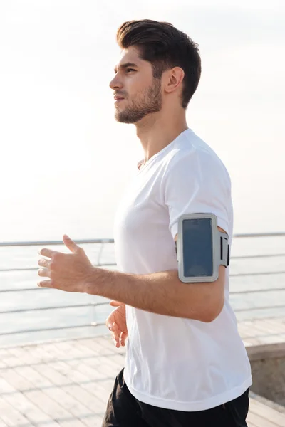 Sportsman with smartphone in armband running on wooden terrace