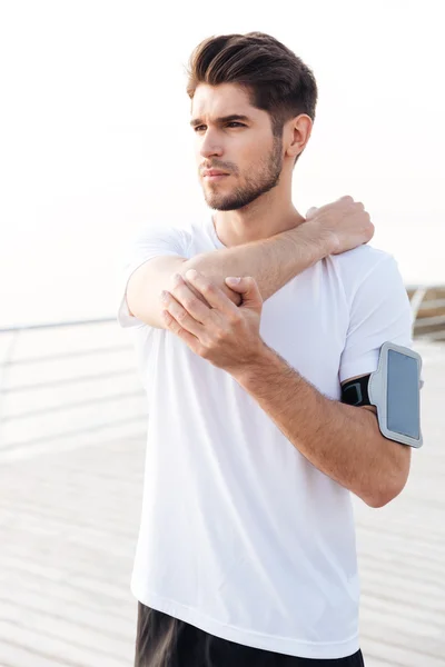 Man athlete with mobile phone in armband stretching arms