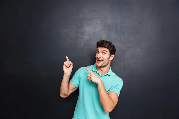 Smiling happy young man pointing fingers away with both hands