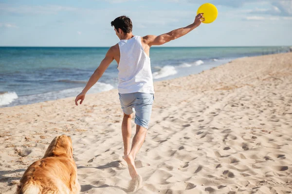 Handsome man playing with his dog on the beach