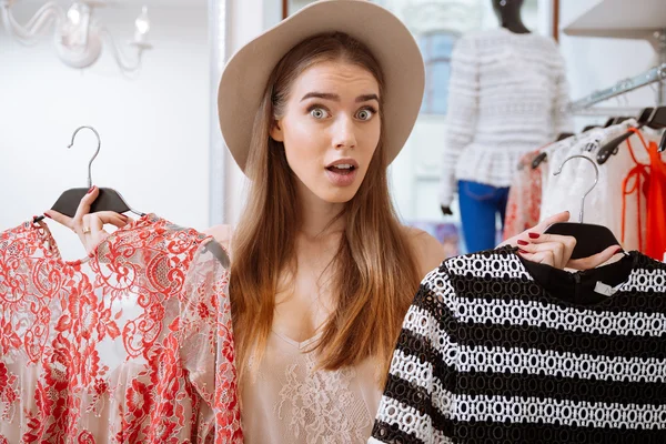 Confused woman doing shopping and choosing dress in clothing store