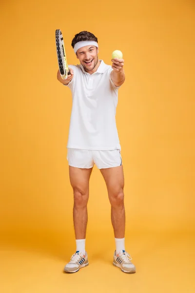 Cheerful young man tennis player giving you ball and racket