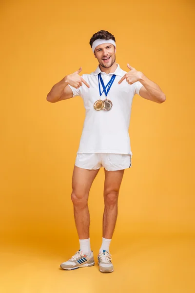 Happy confident young man athlete with medals pointing on himself