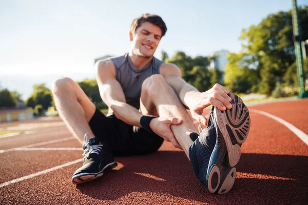 Young male runner suffering from leg cramp on the track