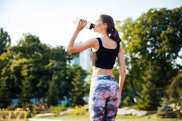 Female athlete drinking from water bottle after workout at stadium