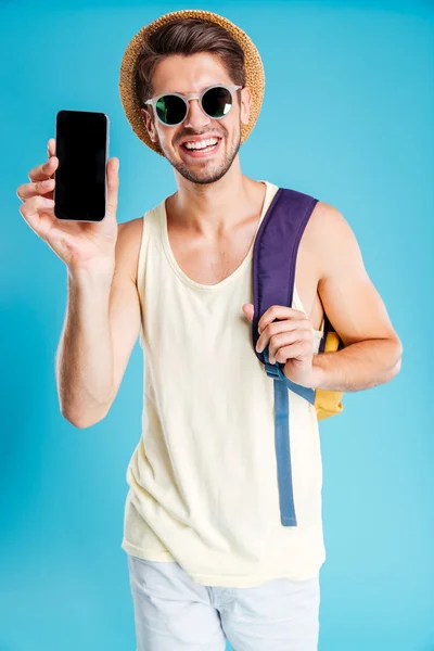 Happy young man with backpack showing blank screen mobile phone