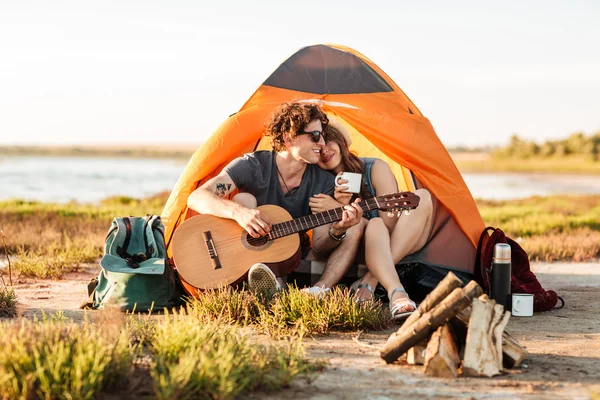 Portrait of a man playing guitar for his girlfriend camping