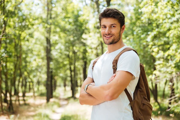 Happy confident young man standing with arms crossed in forest
