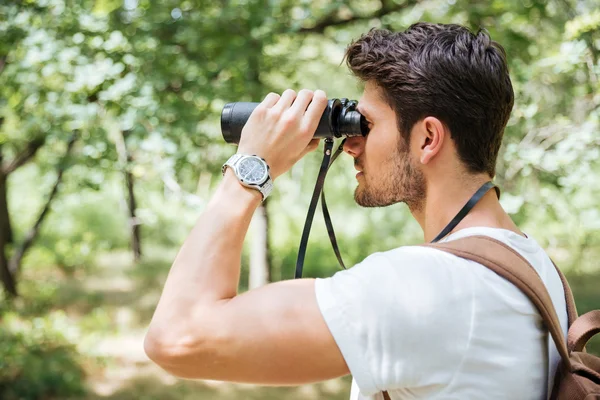 Man with backpack looking through binoculars outdoors