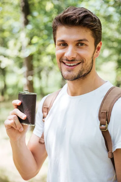 Cheerful young man standing and holding flask in forest